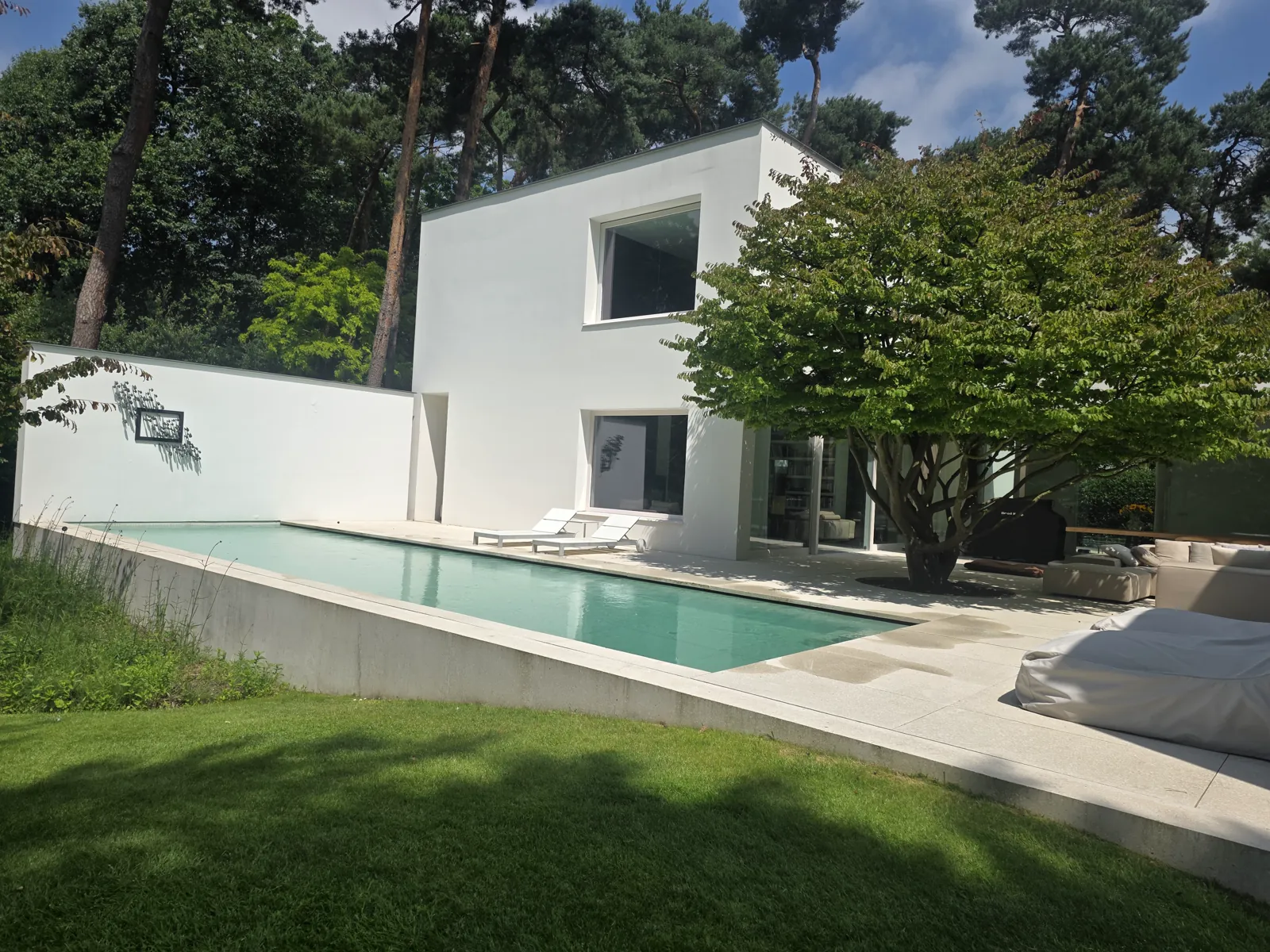 Langwerpig zwembad met lichte rand en terras naast een moderne witte woning