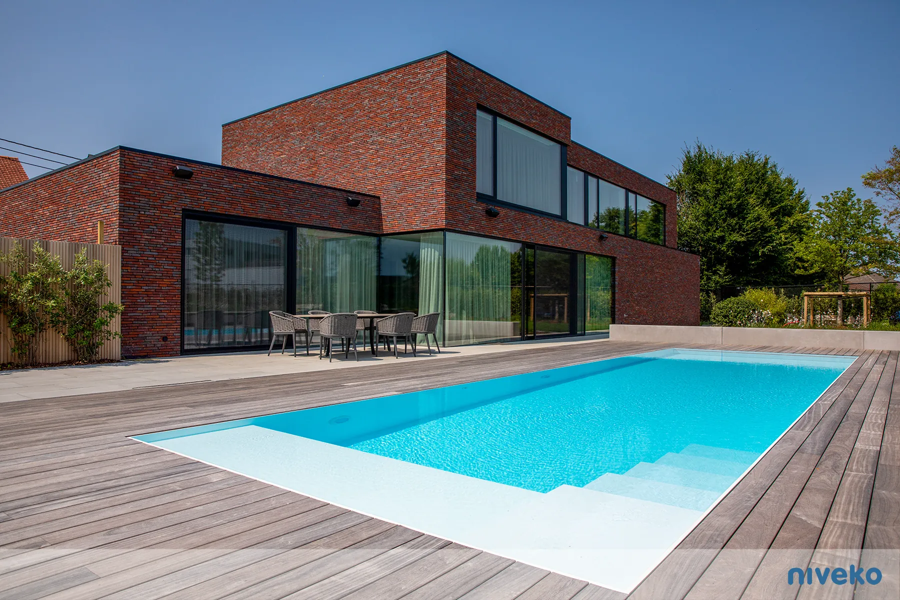 NIVEKO Evolution zwembad met lichte rand en houten terras bij een bakstenen woning