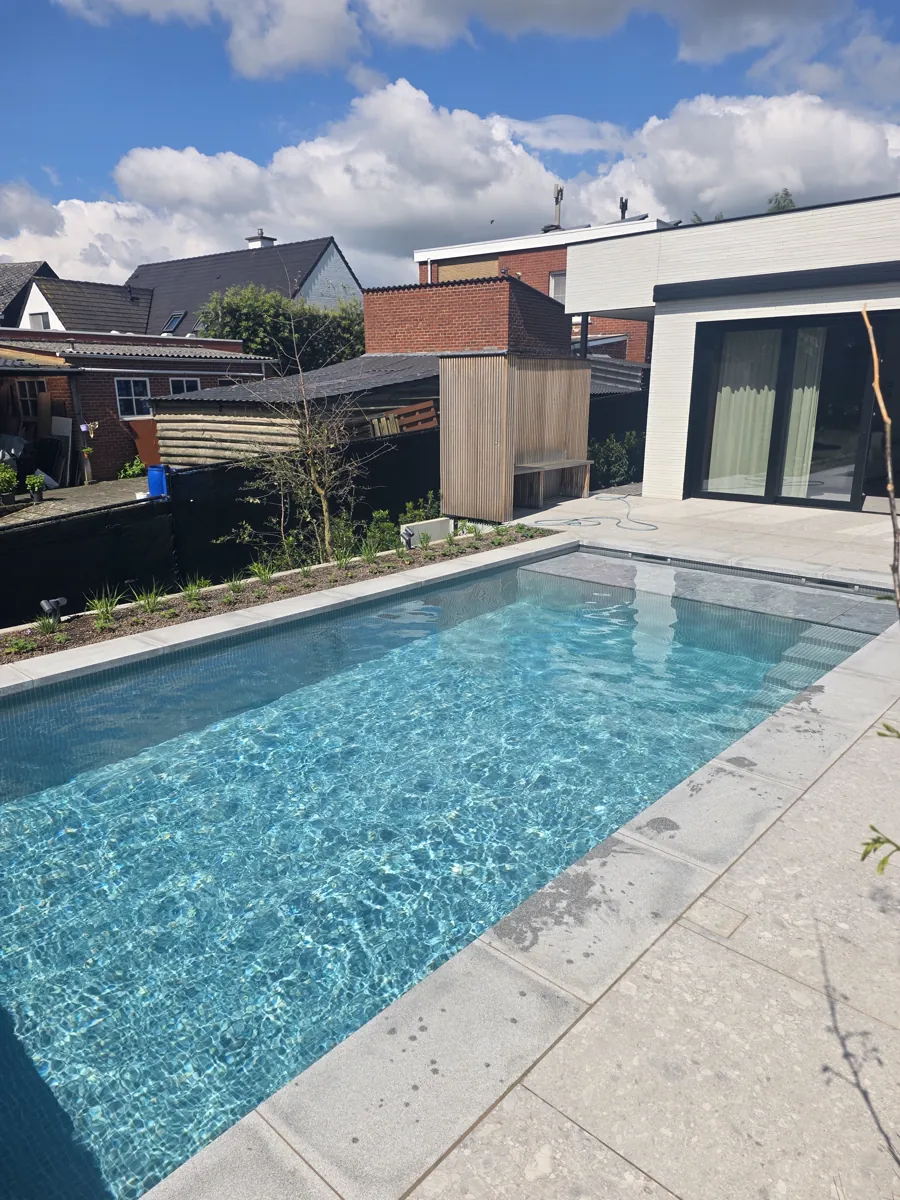 Zwembad met lichte boordstenen en terras bij een moderne woning